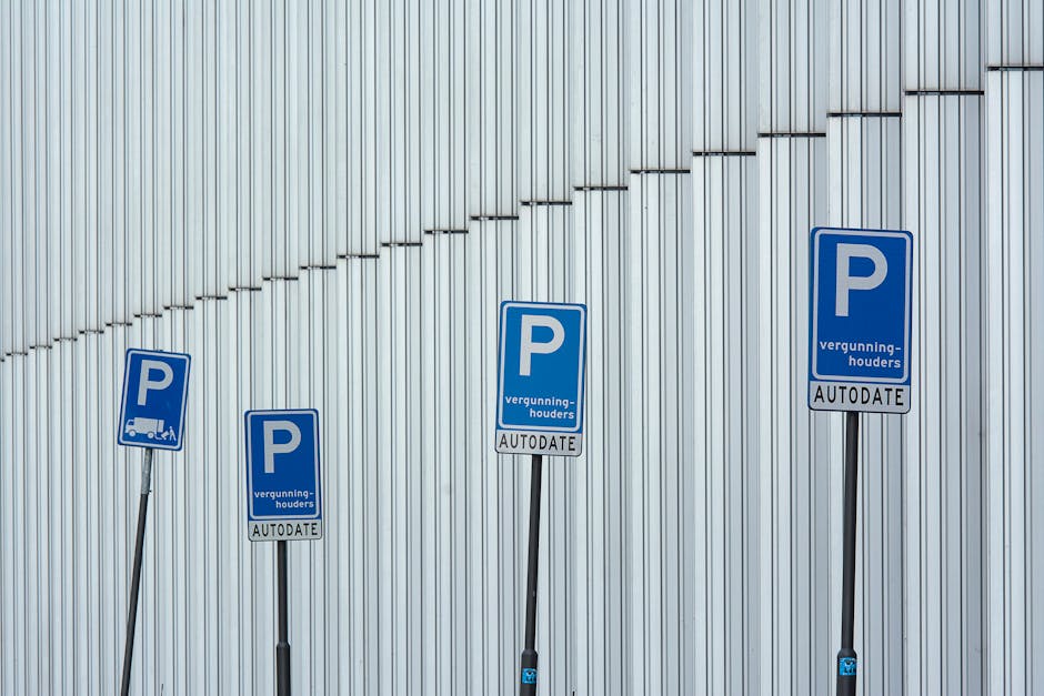Four blue parking signs with white lettering are mounted on black metal poles in front of a corrugated metal wall. The signs display the letter 'P' indicating parking, along with additional text in a